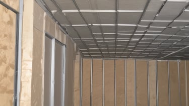 An interior space with walls covered in a dense arrangement of blue, pyramid-shaped acoustic foam panels arranged in a uniform pattern. The perspective creates a visual effect of depth and texture, with lighting that casts shadows across the surfaces.