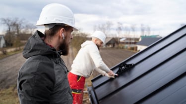 Professional roofing contractors in hard hats installing a black metal roof on a residential house.