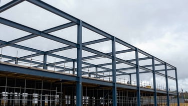 Clean, wide-angle architectural photography of a modern commercial construction site in Newcastle, Northern European / British setting. Features high-quality steel structure work and scaffolding against a bright, overcast sky. Professional, robust atmosphere with steel blue and dark charcoal tones.
