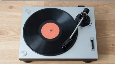 Top-down view of vinyl records and a high-end turntable on a minimalist light wood table, pale blue accents, clean and stylish.