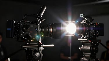 Anamorphic lens flare effect across a dark film set, professional cameras visible in silhouette, professional filmmaking atmosphere.