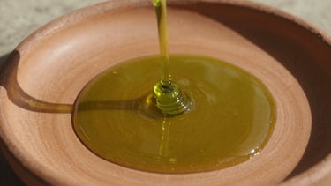 Extreme macro shot of thick, vibrant green olive oil pouring onto a rough terracotta plate, harsh Mediterranean sunlight, deep shadows, 35mm film