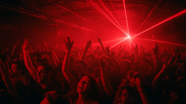 Packed underground club room in Tel Aviv, low ceiling, red strobes, crowd with hands raised, 35mm film