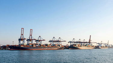 Wide panoramic view of a bustling, brightly lit deep-water port terminal at golden hour, container ships docked, cranes actively moving cargo, expansive sky, low horizon, crisp ocean blues and steel greys, sharp focus, wide-angle lens