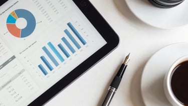 An overhead shot of a clean desk featuring a tablet displaying professional data graphs, a fountain pen, and a cup of coffee. The aesthetic is modern and organized, using navy blue and off-white colors. High-impact professional atmosphere.