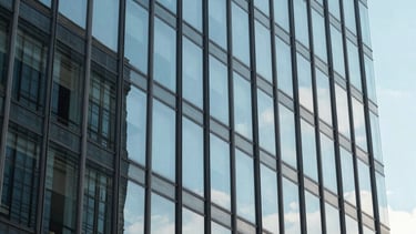 A close-up of a glass facade of a modern corporate building reflecting a clear blue sky. The lighting is bright and natural. The image represents transparency and modern strategic insight.