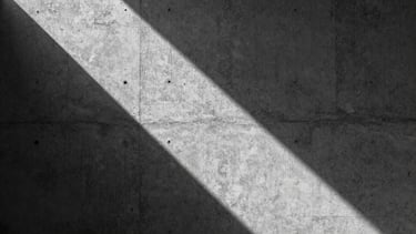 Extreme close-up of raking natural light on a textured concrete wall, dramatic diagonal shadow, minimalist architectural composition