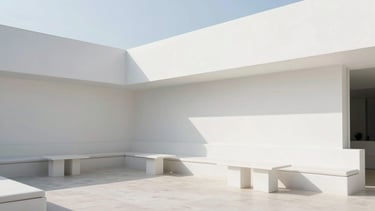 Wide architectural shot of the serene outdoor lounge, clean white walls, minimalist seating, soft shadows, bright natural daylight