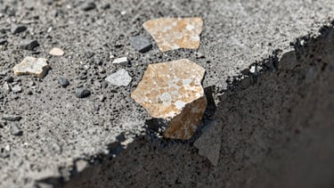 Extreme close-up macro of polished concrete aggregate surface, north daylight illumination revealing champagne-toned stone inclusions, dark graphite matrix surrounding each fragment, shallow depth of field on the nearest plane, no text or human elements