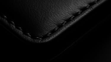 Macro close-up of a flawless black leather executive folio edge, showing pristine hand-stitched details, sharp directional chiaroscuro lighting, deep obsidian tones.