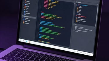 A professional photograph of a laptop screen showing a real-time multiplayer networking console with lines of code. Moody navy and purple lighting.
