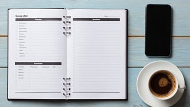 A flat lay photography of social media planning tools: a planner, a smartphone, and a cup of Turkish coffee on a light blue wood surface. Professional and organized. Turkish / Aegean Coast.