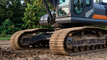 Close-up, low-angle heroic shot of a clean, branded excavator's tracks and lower body, operating on freshly graded earth, crisp morning daylight, deep forest green and charcoal gray tones, sharp details, 35mm.
