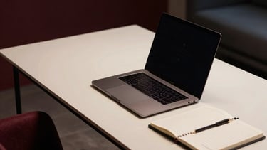 A high-end, professional workspace in a Southern European urban setting, featuring a minimalist desk with a sleek laptop and notebooks. The scene is captured in low-key lighting with deep shadows and warm cream highlights. Accents of burgundy and dark blue-grey appear in the decor, creating a sophisticated and strategic consulting atmosphere.