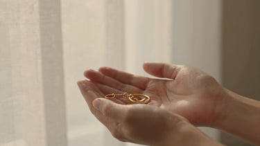 Close-up of hands holding a delicate handcrafted gold keepsake, soft warm golden-hour window light, textured linen background, shallow depth of field, 35mm photography