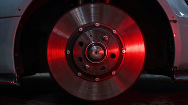 Tight macro shot of a glowing red brake rotor on a race car wheel, dark garage background, dramatic lighting, motion blur.