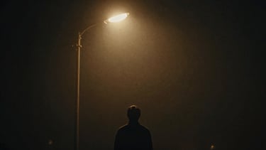 Anamorphic cinematic film still of a lone figure under a warm tungsten streetlamp, heavy fog, deep obsidian shadows, 35mm grain