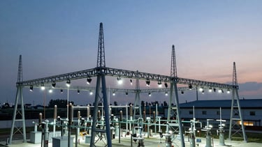 Aerial view of a modern energy substation with complex steel structures against a clear twilight sky, illuminated by cool white security lights.