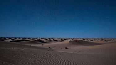 A wide photography shot of a North American desert landscape at night under a clear starry sky, lit with an artificial steel blue cinematic glow to create a speculative sci-fi atmosphere.