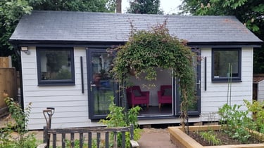 Modern white garden room with black window frames and a climbing plant archway.
