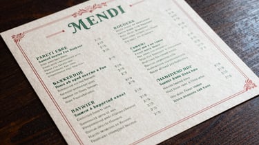 A top-down shot of a beautifully designed menu on parchment paper, featuring forest green typography and crimson accents, resting on a dark wood table.