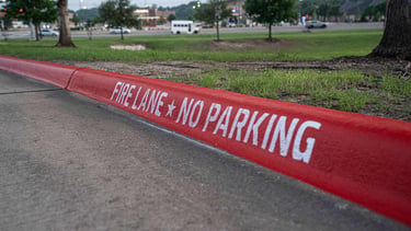 Red painted curb with white Fire Lane No Parking stencil text on a paved street.