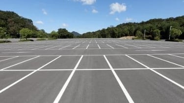 Empty asphalt parking lot with white painted lines under a blue sky with hills.