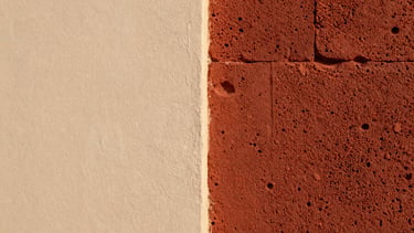 Macro detail of hand-polished lime plaster wall meeting a raw laterite stone block, showing contrasting textures of smooth white and porous red earth, soft side light.