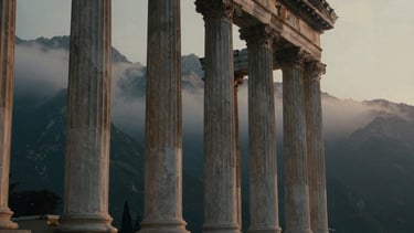Dramatic low-key photography of towering Doric columns emerging from misty mountain peaks at dawn, weathered marble textures, golden-hour side light, cinematic 35mm film