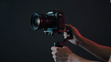 Close-up of hands adjusting a high-end camera rig on a gimbal, dark studio environment, dramatic directional lighting
