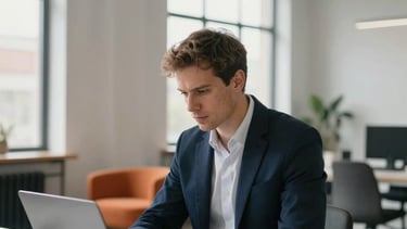 A focused solo entrepreneur in a sharp navy blazer working in a bright, modern European loft office. He is managing a recruitment workflow on a sleek laptop and a smartphone. The background features minimalist furniture, a hint of orange decor, and large industrial windows with soft daylight. Professional photography, clean lines, high contrast.