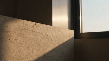 Tight macro-detail of warm travertine stone showing natural organic textures, contrasted against a sharp brushed titanium structural frame, dramatic side lighting, 35mm.