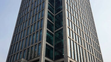 Wide architectural angle of a modern concrete and glass financial skyscraper in Delhi NCR, sharp shadows under bright corporate daylight, deep navy and emerald tones, 35mm