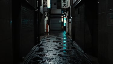 Dark cinematic photography of high-contrast Tokyo alleyway at night, desaturated tones with subtle neon cyan wet pavement reflections, 35mm anamorphic frame