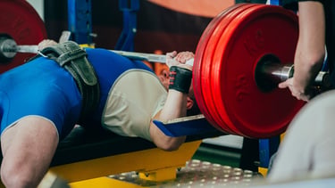 A powerlifter performing a heavy bench press with red weight plates and a lifting belt.