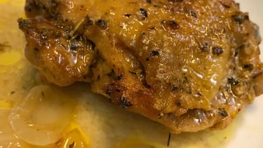 Juicy baked chicken thigh on a white plate with broth and onions