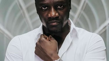 Singer Akon wearing a white shirt and luxury watch while posing in a tunnel.