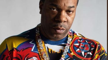 Portrait of rapper Busta Rhymes wearing a colorful graphic sweater and a diamond chain.
