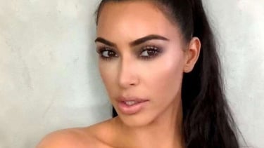 Kim Kardashian posing with a high sleek ponytail and glamorous smokey eye makeup look.