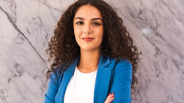 Professional headshot of a woman with curly hair wearing a blue blazer and white top, standing with 