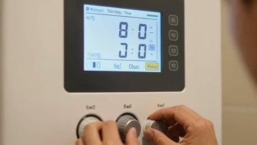 A close-up shot of a modern boiler control screen displaying perfect temperature settings. A professional technician's hand is softly adjusting the dials in a household setting in Tekirdağ / Thrace, Turkey. Warm color temperature.