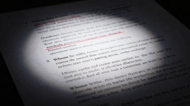 Dramatic chiaroscuro photograph of hand-written speech edits under a single direct spotlight, red ink corrections on white paper, deep charcoal shadows.