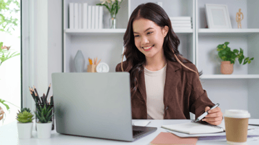 Chica sonriente sentada en un escritorio con un ordenador portátil y una libreta