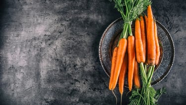 Des carottes dans une vieille assiette en fer avec un fond gris foncé.