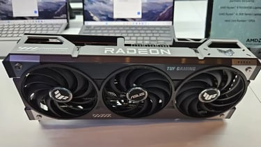 placa de video radeon encima de una mesa , se ve atras 2 notebooks encendidas