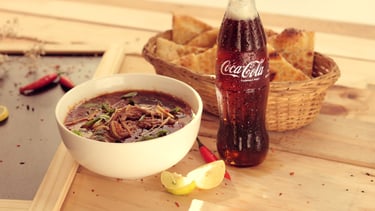 Product photography of a bowl of noodles with a Coca-Cola bottle and ingredients on wooden table