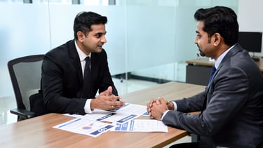 Two male professionals in suits having a business meeting or job interview at an office desk.