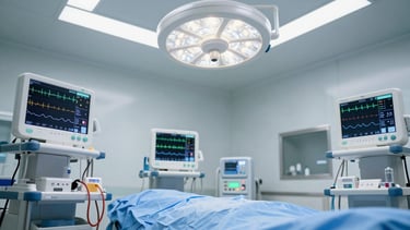 Wide panoramic view of an anesthesia monitoring station in a surgical suite, EEG electrode leads and waveform display screens visible in the foreground, cool clinical overhead lighting, no patients or clinicians present, stark and precise