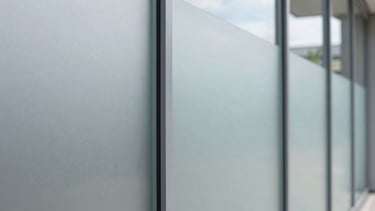 Tight macro shot of the edge of a frosted glass partition, showing the precision cut of the film and its seamless integration with the glass, crisp architectural photography, bright natural daylight, clean glass reflections, cool grey and blue tones, 35mm lens.