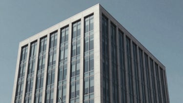 A sharp, professional photography shot of a modern North American office building exterior with clean glass lines and a light gray facade, set against a clear blue-gray sky. Minimalist architectural style reflecting business sophistication.